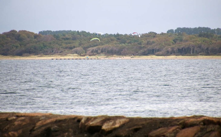 På söndagen lyste kitesurfarna med sin frånvaor i Båstads hamnområde. Men ett tränat öga kunde se att de startar i Hemmeslöv. Bilden är tagen med zoomobjektiv. Foto: Peter Jakobsson